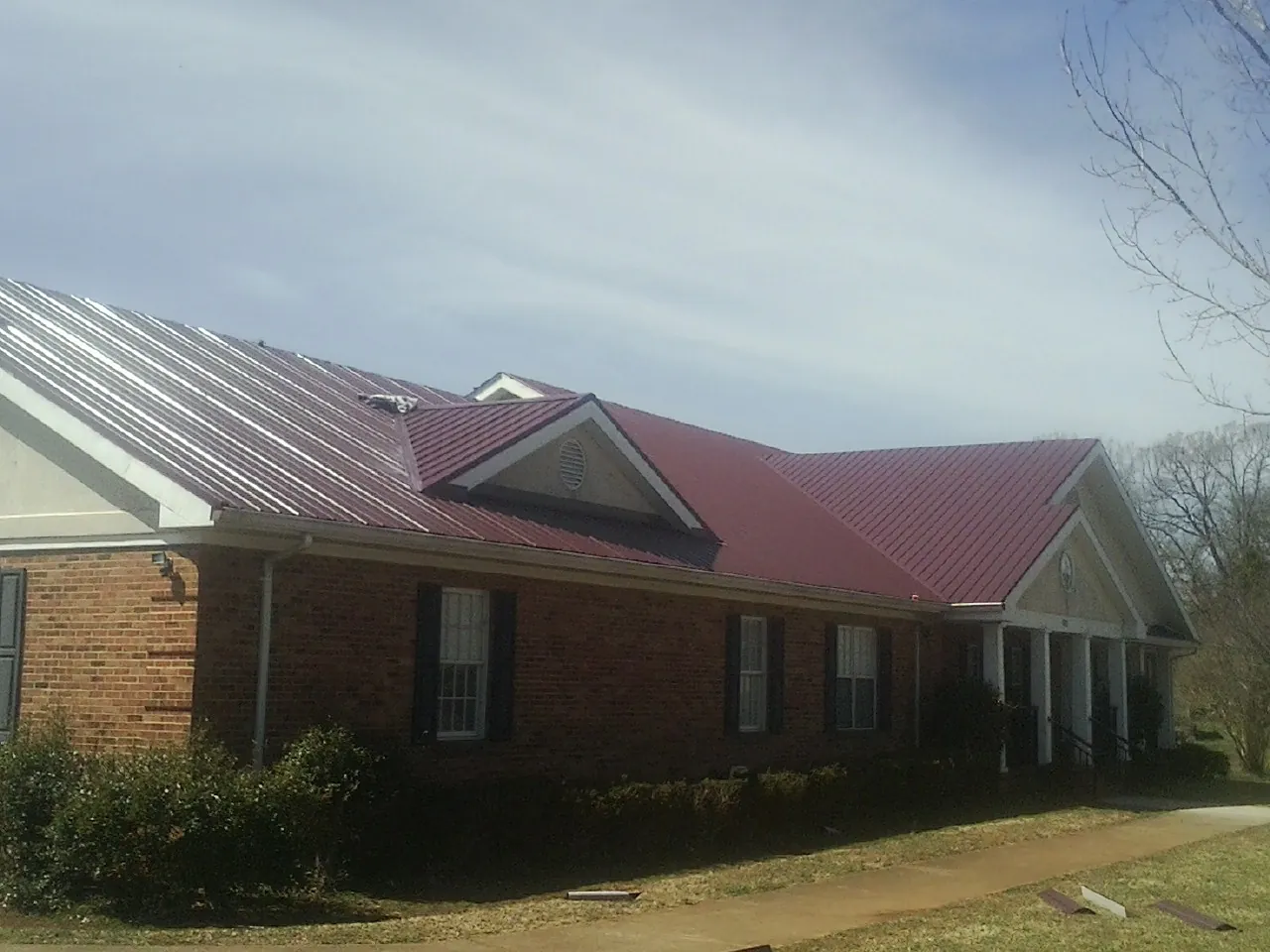 Red metal roof with gabled entries on a long brick building, from a Hail Damage Roof Repair job in Watsonville