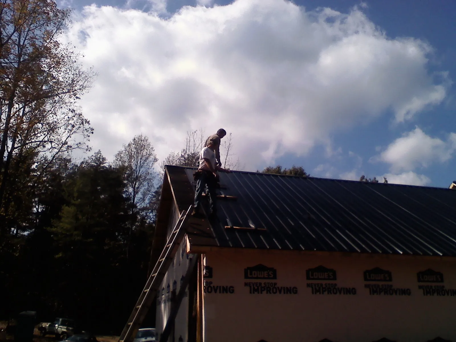 Roofer fastening dark metal panels high against a cloudy sky, from a Roof Inspection job in Watsonville